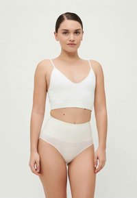 Biely crop top s tenkými ramienkami skombinovaný s high-waisted spodkami, s hladkou textúrou a minimalistickým dizajnom.