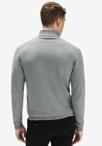 Harmaa neulepusero, jossa on ribattu poolokaulus, kapea malli ja pitkät hihat, näkyy takaa. Sileä pinta, jossa on hienovarainen ompelutaito.