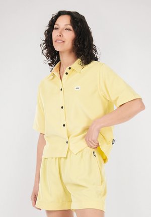Yellow button-up short-sleeve shirt and matching shorts in lightweight fabric. Features black buttons and a small logo patch on the shirt.