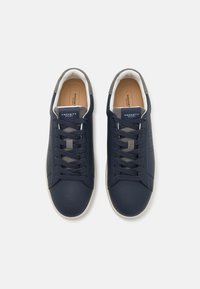 Marina blå sneakers med överdel i slät läder, grå detaljer på tungan och hälen, samt krämvitt gummisulor. Innehåller platta skosnören och branding.