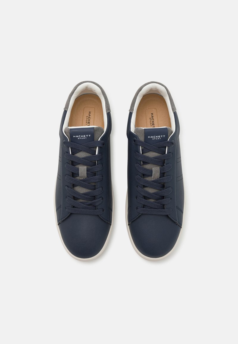 Baskets bleu marine avec un dessus en cuir lisse, des accents gris sur la languette et le talon, et des semelles en caoutchouc blanc crème. Elles possèdent des lacets plats et une marque.