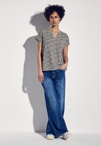 Top a maniche corte con motivo bianco e nero e scollatura a V, abbinato a jeans larghi blu chiaro e sneaker bianche. Sfondo con superficie piatta.