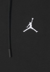 Tessuto di felpa nera con una texture liscia, caratterizzato da un logo Jumpman ricamato in bianco. Include un dettaglio con cordoncino al collo.