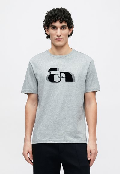 Sivé bavlnené tričko s okrúhlym výstrihom, na prednej strane s čiernym abstraktným logom. Krátke rukávy a voľný strih.