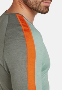 Herrtröja i ljusgrön med texturerad tyg, med ett iögonfallande orange vertikalt rand längs axeln för kontrast.