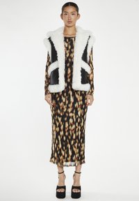 Gilet in pelliccia sintetica bianca e nera con tasche laterali indossato sopra un lungo abito aderente a fantasia nei toni del nero, arancione e marrone.