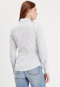 Chemise rayée boutonnée en bleu clair et blanc, en coton, dotée d'un col classique, de manches longues avec fentes aux poignets, et d'un ourlet arrondi.