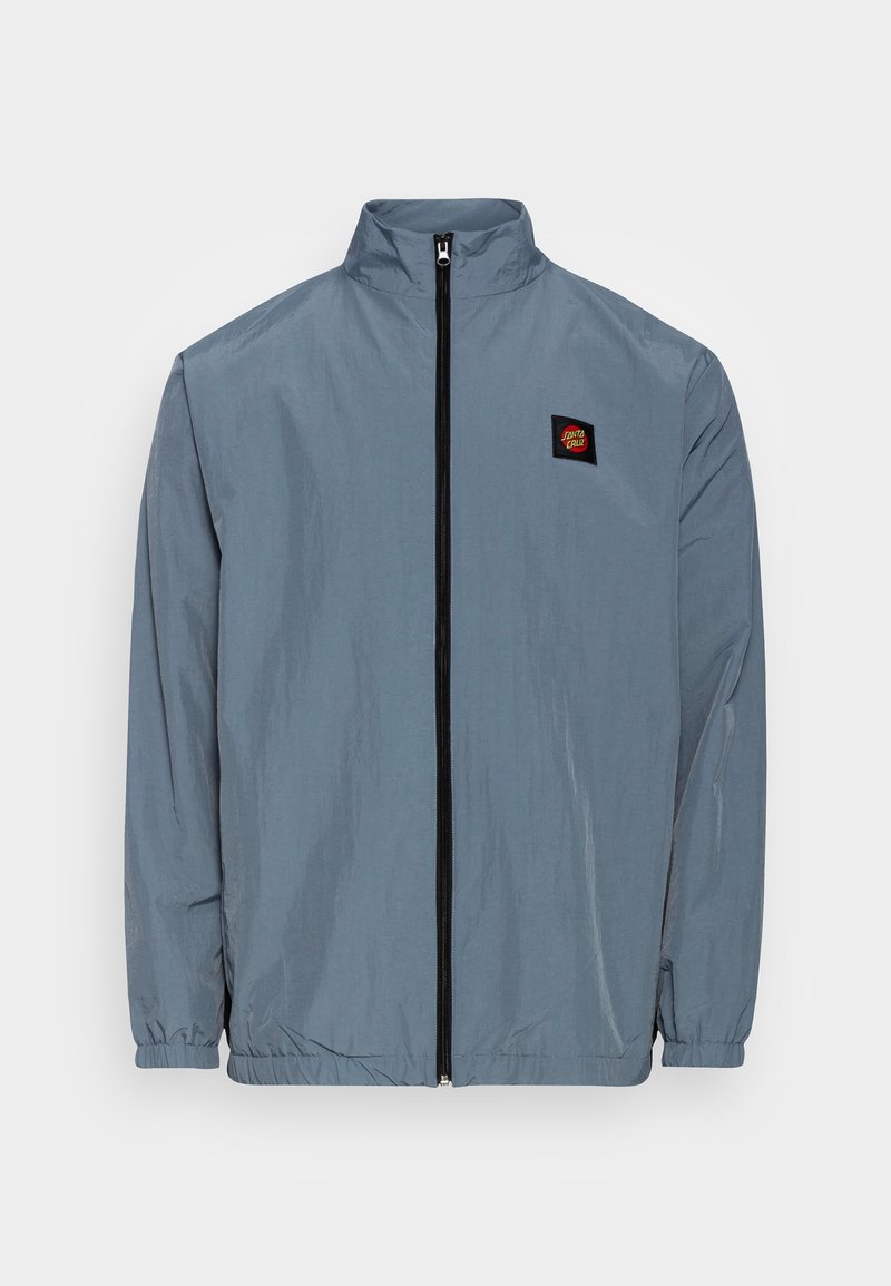 Letvægts, langærmet jakke i skifergrå med høj krave, sort lynlås, elastiske manchetter og et lille logo-patch på brystet.