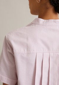 Lichtroze shirt met korte mouwen, voorzien van verticale witte strepen, een detail met een rugplooitje en een zachte kraag. Gladde, katoenachtige textuur.