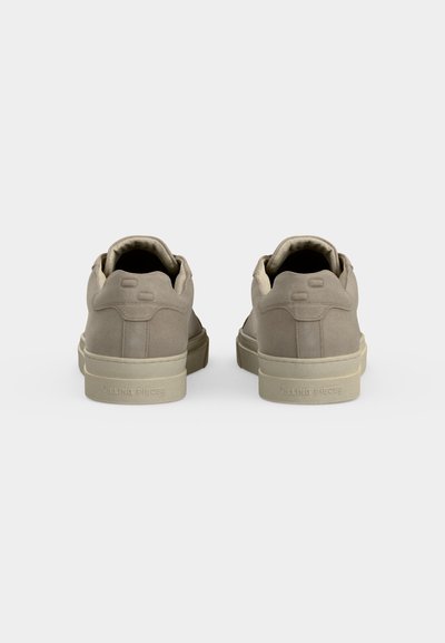Paire de baskets basses beige vue de dos, avec des semelles épaisses et des collerettes rembourrées sur fond blanc uni.
