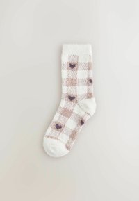 Puszyste skarpetki do kostek w białym kolorze z brązowym wzorem w kratę, zdobione małymi ciemnymi sercami. Miękka tekstura z jednolitym kolorem ściągacza.