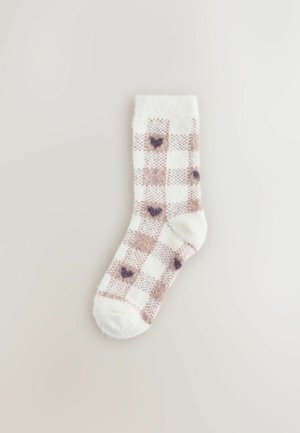 Plyšové kotníkové ponožky bílé barvy s hnědým kostkovaným vzorem, které obsahují malé tmavé srdce. Měkká textura se jednobarevným lemem.