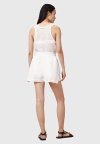 Top bianco senza maniche con una texture trasparente, abbinato a pantaloni corti bianchi leggeri con vita elastica, indossato con sandali neri.