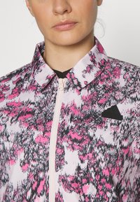 Giacca leggera con zip, in un motivo astratto rosa e nero. Presenta un colletto e un accento con il logo adidas sul petto.