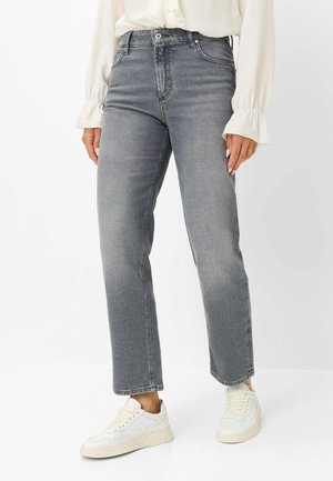 Person iført grå, højtaljede jeans med lige ben, hvide sneakers og en cremefarvet bluse med lange ærmer og flæsekant ved manchetterne.