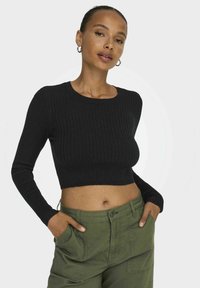 Fekete bordázott crop top hosszú ujjal, kerek nyakkivágással és testhezálló dizájnnal. Olíva zöld cargo nadrággal párosítva, amely oldalra elhelyezett zsebekkel rendelkezik.