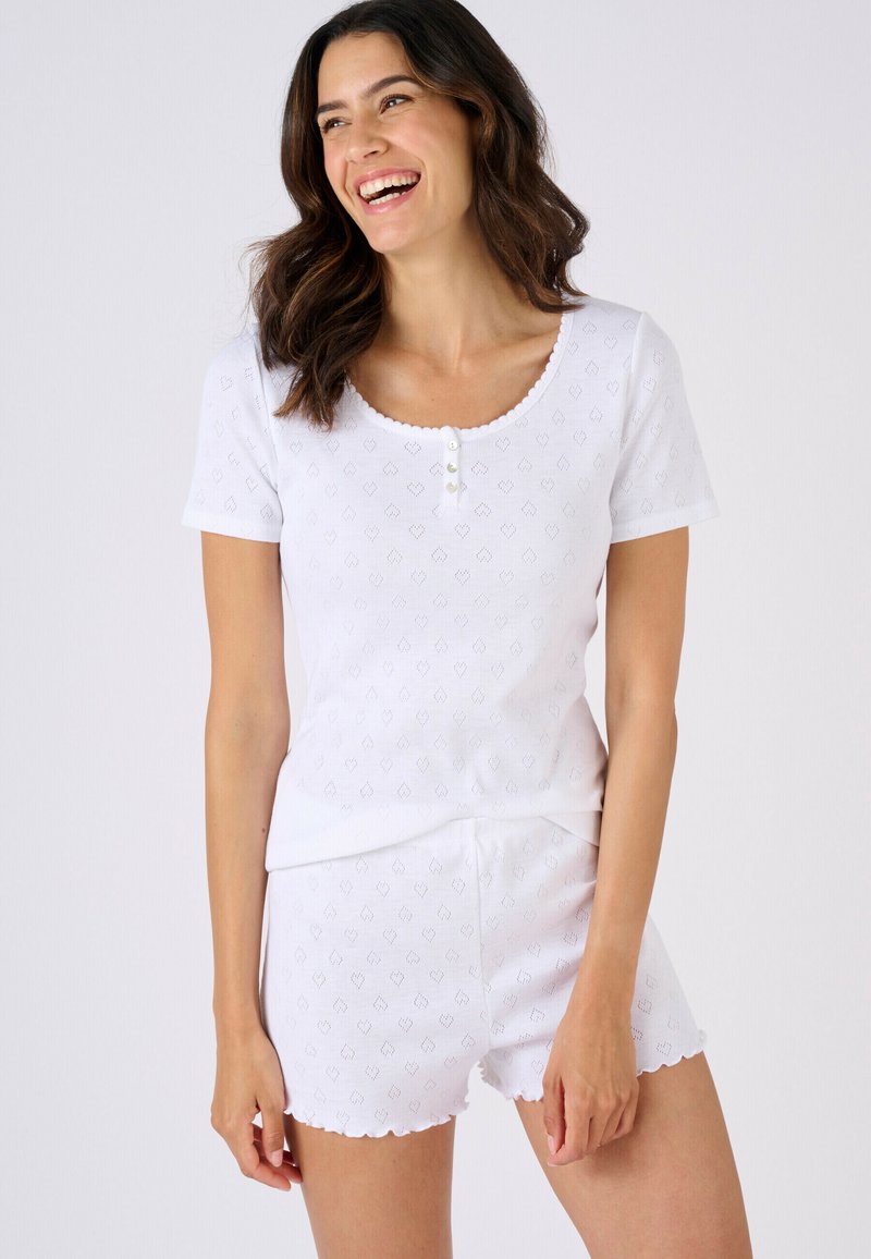 Conjunto blanco de top de manga corta y pantalones cortos con borde festoneado, que presenta un patrón texturizado de pequeños corazones y cierre frontal con tres botones.