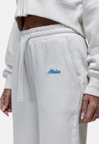Witte fleece joggers met een elastische tailleband, zijzakken en geborduurde tekst in het blauw. Zachte textuur en een relaxte pasvorm.