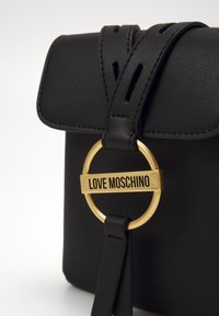 Borsa nera in finta pelle con una patta arrotondata, caratterizzata da un'accento in metallo dorato a forma circolare e una placca incisa con "LOVE MOSCHINO."