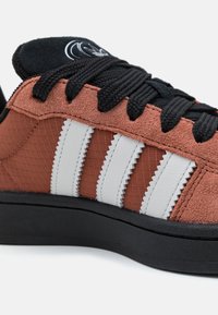 But sneaker w kolorze rdzy z białymi zygzakowymi paskami, czarnymi sznurowadłami, czarną podeszwą oraz czarnym językiem z białym logo.