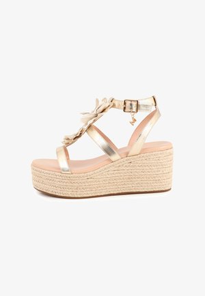 Sandalias de cuña metálicas doradas con suela de yute trenzado, detalles florales y correas en el tobillo. Punta redonda con un forro interior liso de color beige claro.