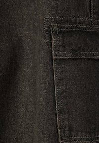 Tessuto in denim nero con una superficie texturizzata. Presenta una tasca cucita sul lato destro, evidenziando una cucitura rinforzata.