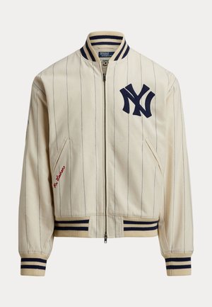 Hellcremefarbene Baseballjacke mit marineblauen Nadelstreifen. Verfügt über ein marineblaues "NY"-Logo, gerippten Kragen, Bündchen und Saum. Beinhaltet Seitentaschen und rote Stickereien.