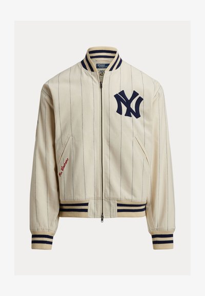 Helebeežikreemjas baseball-jakk mereväesiniste varrastega. Sellel on mereväesinine "NY" logo, sooniline krae, mansetid ja alumine äär. Sisaldab küljetaskuid ja punast tikandit.