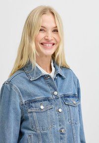 Chaqueta de mezclilla azul claro con un diseño clásico, que presenta botones de metal, dos bolsillos en el pecho y un cuello. Textura suave visible.