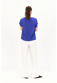 Koninklijk blauwe short-sleeve top met een ontspannen pasvorm, gecombineerd met losse witte broeken en zwarte instapschoenen. Gladde stoftextuur.
