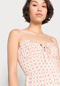 Vestido floral com padrões laranja e branco, decote com pregas, alças ajustáveis e cintura ajustada para uma silhueta justa.