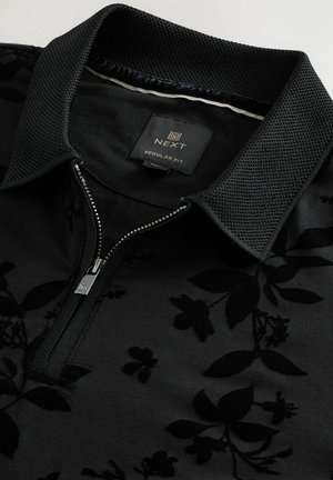 Black zip-up polo shirt featuring a textured collared neckline and a subtle floral pattern embossed on a smooth fabric surface.
