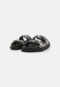 Schwarze Sandalen mit mehreren Riemen, silbernen dekorativen Beschlägen, strukturierten Schnallen und einer dicken, robusten Sohle.