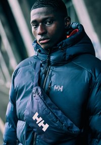 Námořnická péřová bunda s vysokým límcem, se zipem a logem 'HH'. Vybavena odpovídající námořnickou crossbody taškou s jemným leskem.