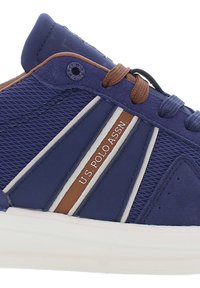 Blå sportskor med en strukturerad mesh-överdel, bruna detaljer, vita ränder och en logotyp. Har runda skosnören och en vadderad krage.