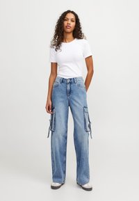 Svetlo modri denim cargo hlače s širokimi nogami, ki imajo stranske žepke, nastavljive vrvice in gumbasto zapiranje. Ujemajoče se s prilegajočo belo majico.