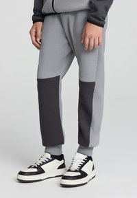 Szare i ciemnoszare dresy o tapered fit, z kontrastowymi panelami i elastycznymi mankietami, w zestawieniu z czarno-białymi sneakersami.