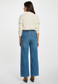 Maglione a coste in cotone avorio, dalla vestibilità casual, abbinato a jeans a gamba larga blu a vita alta. Stivaletti con tacco marroni completano l'outfit.