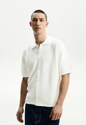 Witte polo met korte mouwen, voorzien van een geprofileerd breiwerk, knoopsluiting en een klassieke kraag, gecombineerd met donkere jeans.