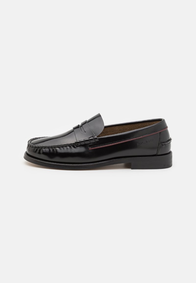 Mocassins en cuir noir avec un bout arrondi, des coutures sur le dessus, un talon bas et une finition lisse. Accents rouges sur le côté.