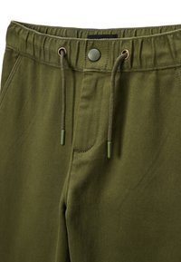 Pantalon vert olive avec taille élastique, cordon de serrage et une seule poche frontale. Présente des accents en métal et une texture douce.