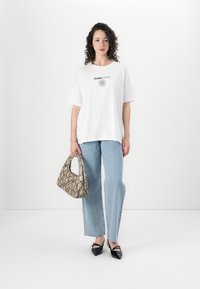 Λευκό T-shirt με μαύρη εκτύπωση, ανοιχτό μπλε τζιν παντελόνι με γυαλάδα, φορτωμένη μπεζ τσάντα και μαύρες γόβες.