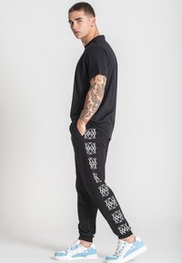 Svart t-shirt, svarta sweatshirtbyxor med vita grafiska mönster och blå och vita sneakers. Slät tygkvalitet, avslappnad passform och avslappnad stil.