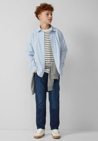 Lichtblauw gestreept overhemd over een grijs gestreept T-shirt, gecombineerd met donkere jeans en witte sneakers. Informele outfit met gelaagde texturen.