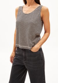 Canotta a righe in cotone bianco e nero con vestibilità rilassata, scollo a U e spalline, abbinata a pantaloni in denim scuro.