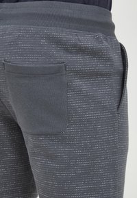 Dark grey jogger pants made of soft material, featuring a ribbed waistband and a back pocket, with a subtle speckled pattern.