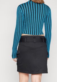 Modrý a černý pruhovaný pletený top s dlouhými rukávy, spárovaný s černou sukní, která má zadní kapsu a strukturovaný pas.