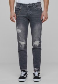 Falmet sorte denimjeans med slitte lapper, kjedetail på lommen og slim fit. Brukt med svart og hvit sneakers.