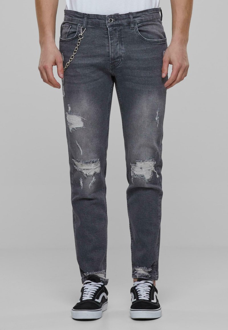 Falmet sorte denimjeans med slitte lapper, kjedetail på lommen og slim fit. Brukt med svart og hvit sneakers.