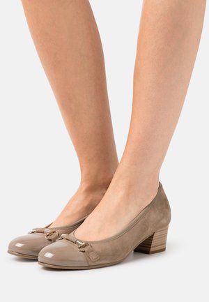 Escarpins beiges avec un bout en vernis brillant et un corps en suede, featuring un petit accent doré à l'avant et un talon empilé.